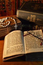reading glasses on the pages of an old book and rosary