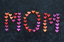 The word MOM written with many little colorful clay hearts on black background