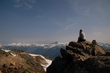 a woman sitting on a rocky peak looking out over mountains 