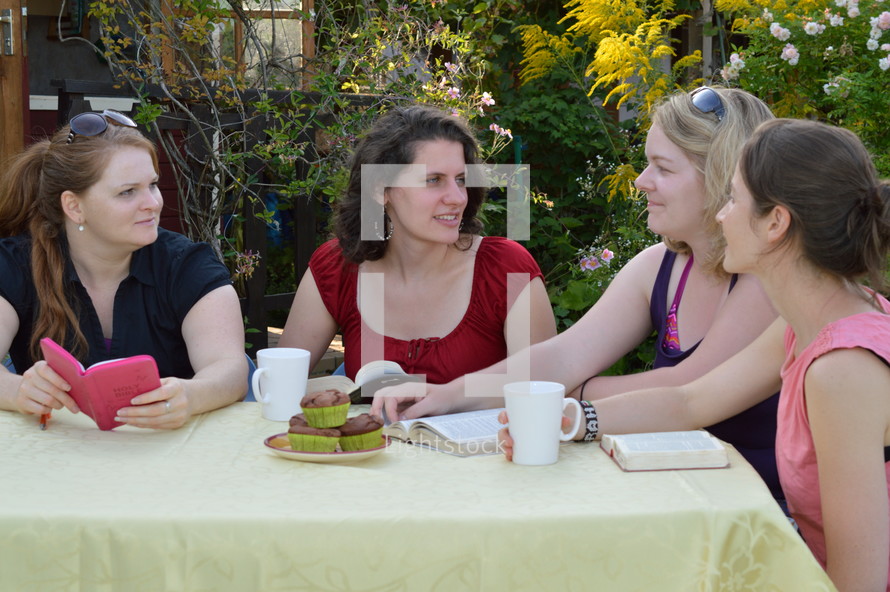 women's group reading scripture together sitting at a table in the garden for a Bible study