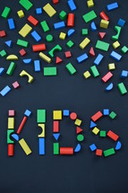 the word KIDS out of colorful wooden toy blocks on black background