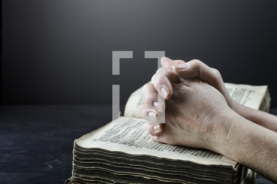 praying hands over an old worn Bible 