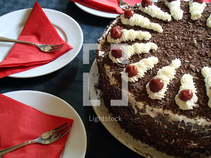 Black forest cake surrounded by plates and napkins ready to be eaten. 
