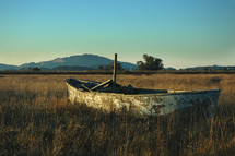 Weathered sailboat in a grassy field.