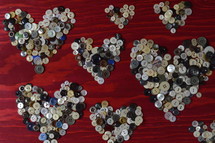 many little buttons shaping hearts on a red wooden background