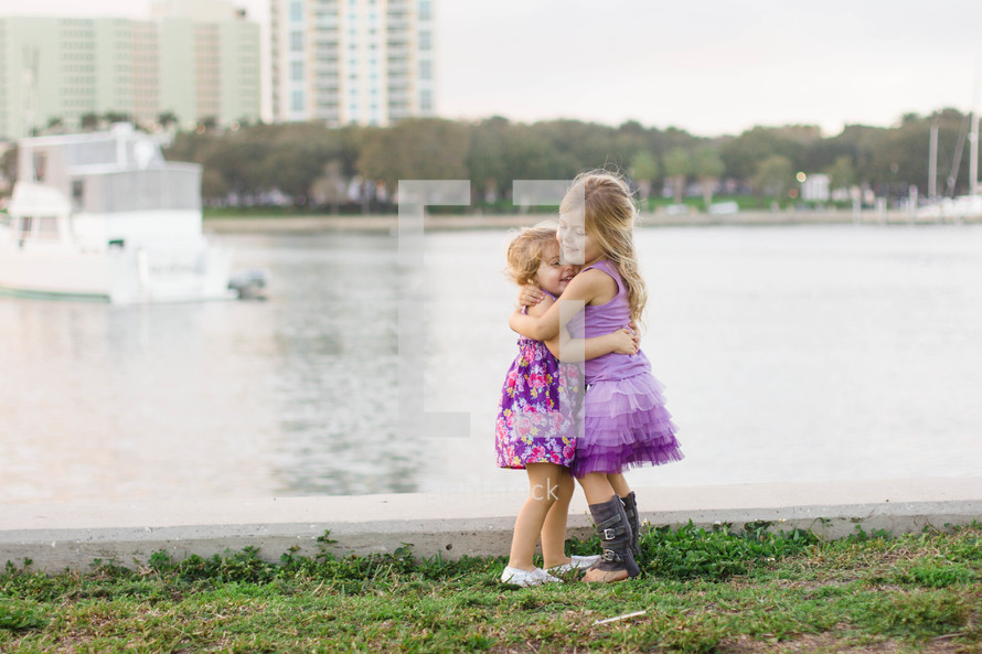 Two young girls hugging standing by a lake