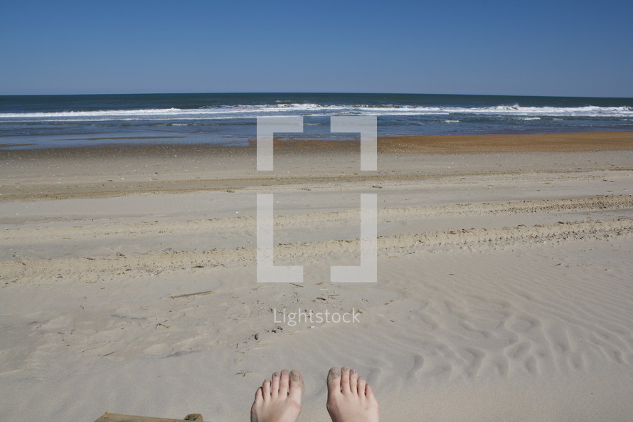 bare feet resting on a sandy beach 