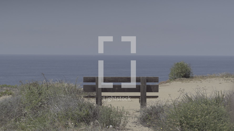 An empty bench on an empty beach overlooking the ocean.