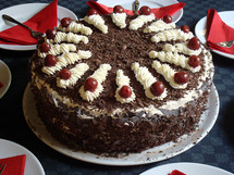 Black forest cake surrounded by plates and napkins ready to be eaten. 
