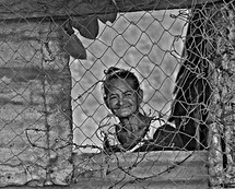 face of an elderly woman behind a chain link fence 