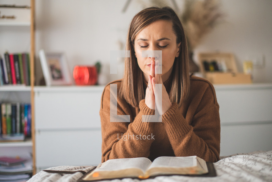 Woman praying with hands folded while reading bible