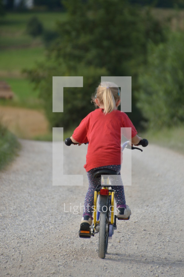 a little girl riding a bike down a gravel road 
