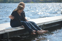 a couple sitting on a dock dangling their feet over the water 
