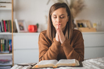 Woman praying with hands folded while reading bible