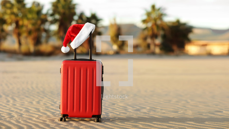 Red suitcase with Santa Claus red hat on handle with tropical sand beach, palms, mountains and sea background. Travel concept for the Christmas holidays and New Year. Place for text. Discounted trips.