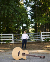 a guitar in front of a man standing near a fence outdoors 