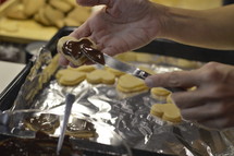 Woman spreading liquid chocolate onto the marzipan layer of Christmas cookies