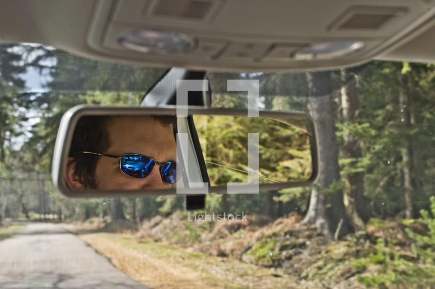 reflection of a man in sunglasses in a rearview mirror