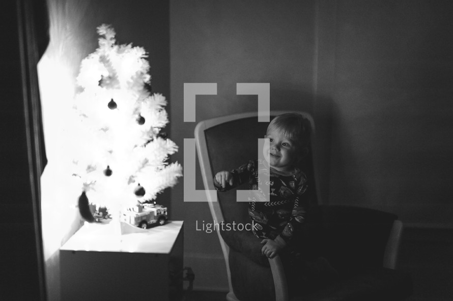 a toddler boy looking at a Christmas tree 