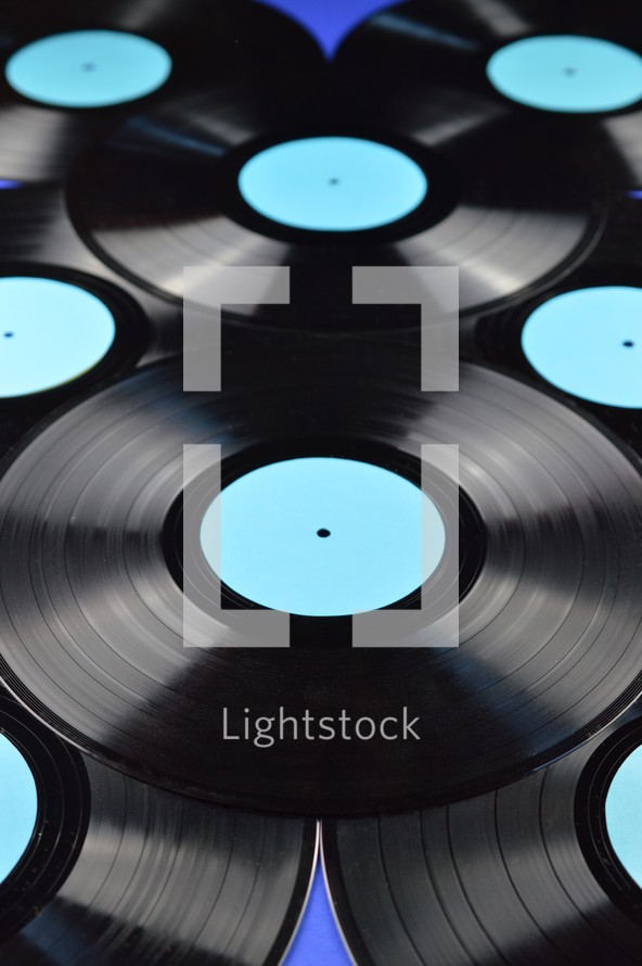 pile of old black vinyl records with blank cyan labels on blue background