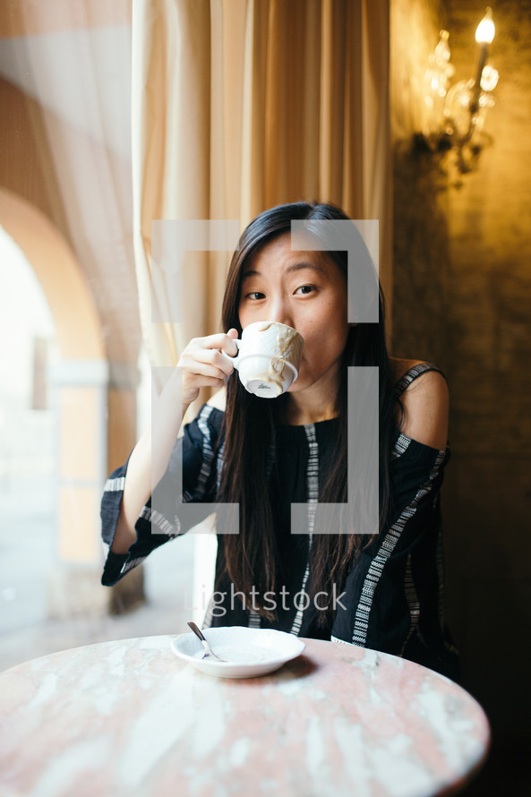 a woman sitting alone at a table drinking coffee 