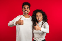 african american couple making thumbs up like sign over red background. Winner. Success. Positive girl and man smiles to camera. 