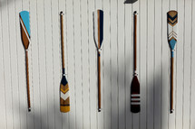 four colourful wooden paddles hangs on a white wall. canoe oars for active water sport. holiday vacation. High quality photo.