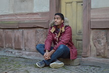 man in a coat sitting in front of a door 
