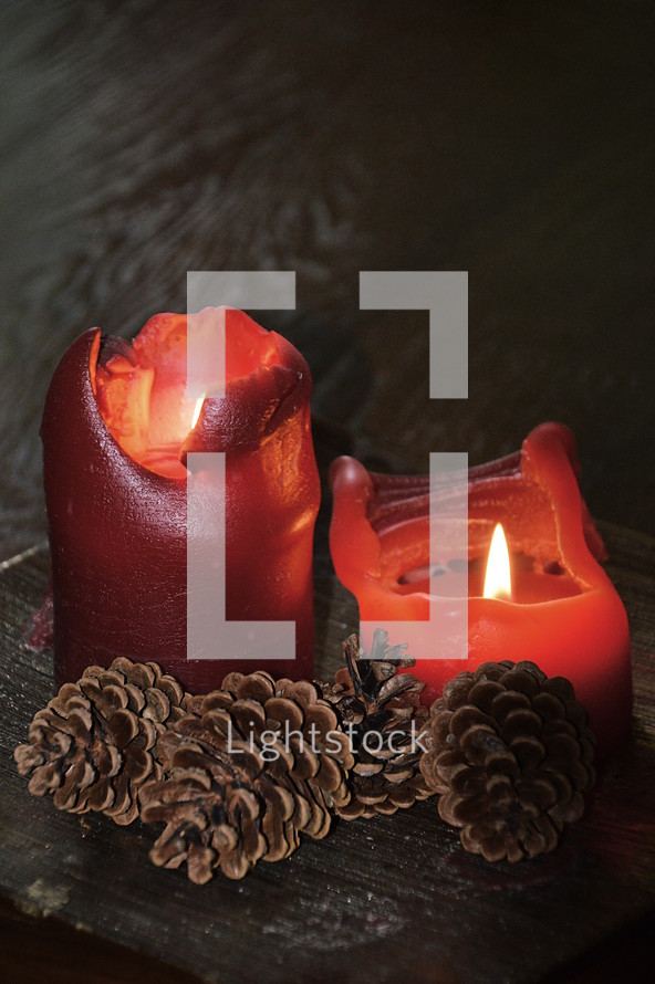 melting wax and flames on red candles and pine cones 