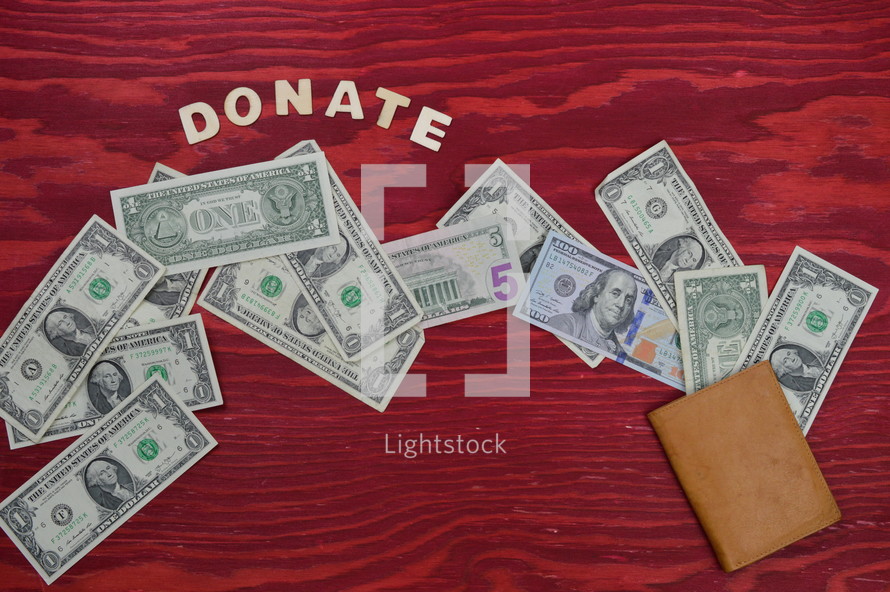 money spilling out from a wallet on a red wooden table with the word donate in wooden letters