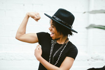An African American woman in a black hat flexing her muscles 