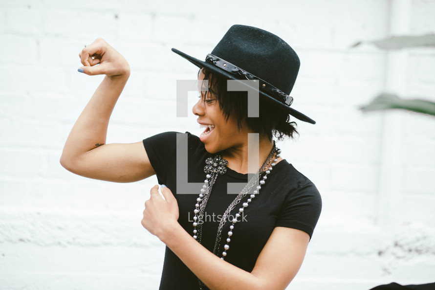 An African American woman in a black hat flexing her muscles 