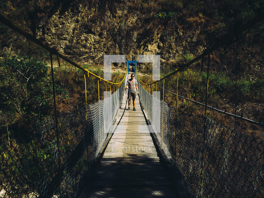 man walking across a swinging bridge 