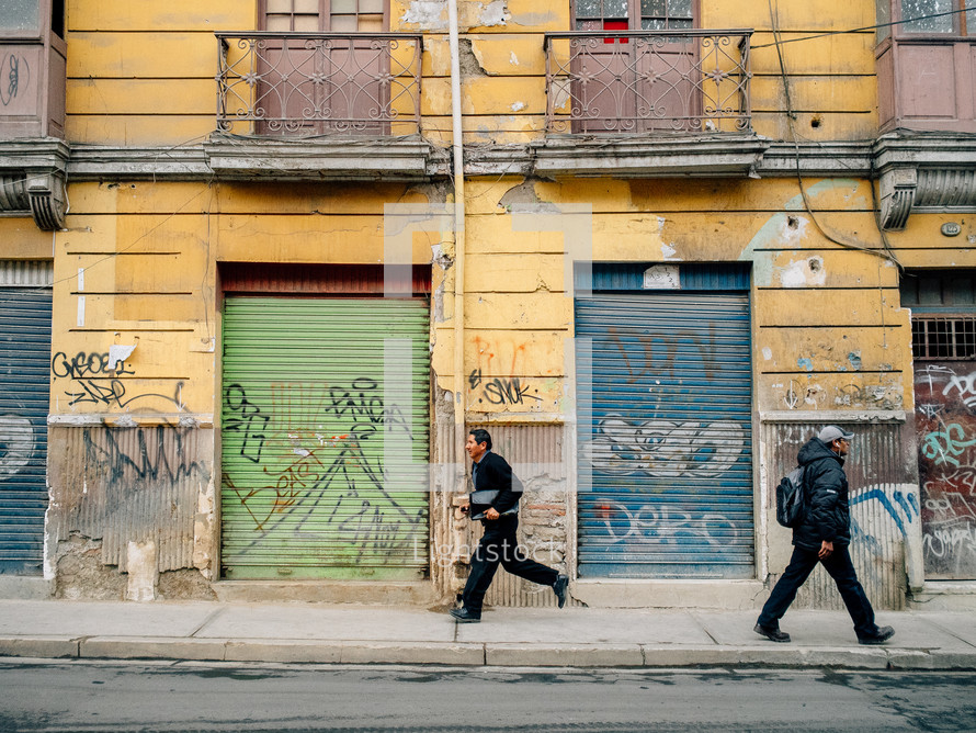Two men walking along a street of colorful buildings and graffiti.