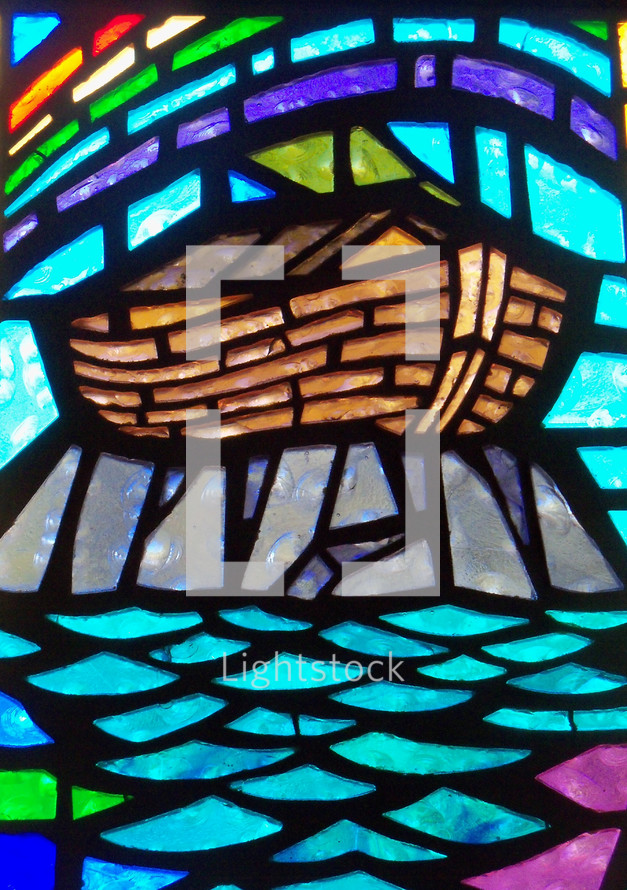 A close-up view of a stained glass window depicting the ark built by Noah resting on dry land surrounded by receding waters and an over arching rainbow showing God's promise to man to never destroy the world by flooding ever again. 