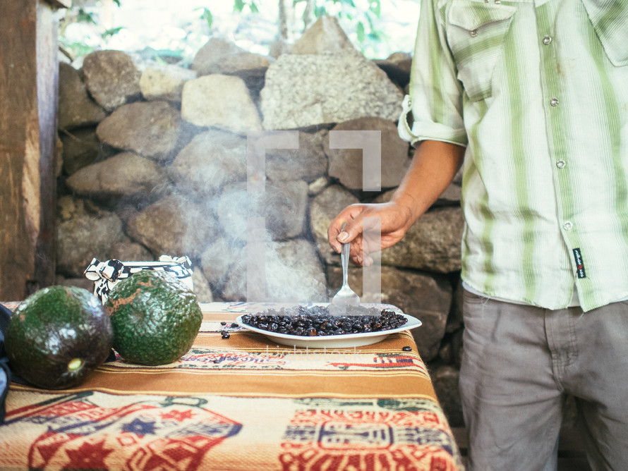 Man stirs a steaming bowl of black beans.