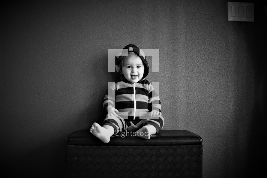 toddler boy sitting on a laundry hamper 