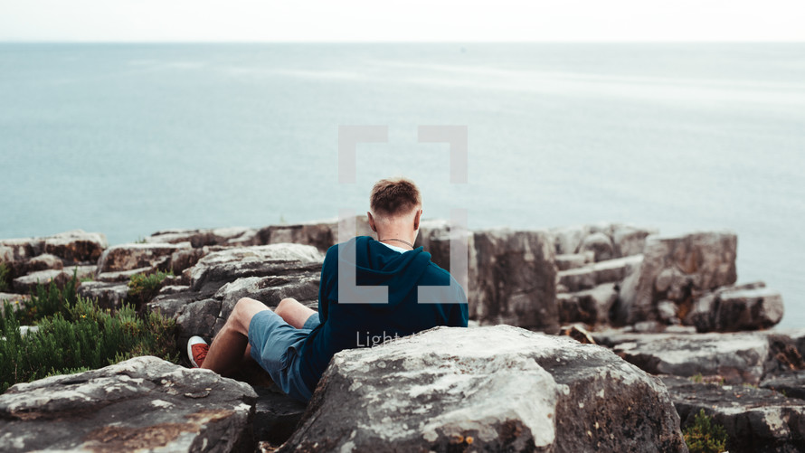 a man sitting on rocks along a shore 
