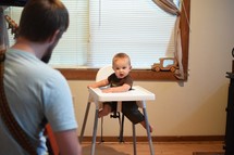 a father playing a guitar to a baby in a highchair 