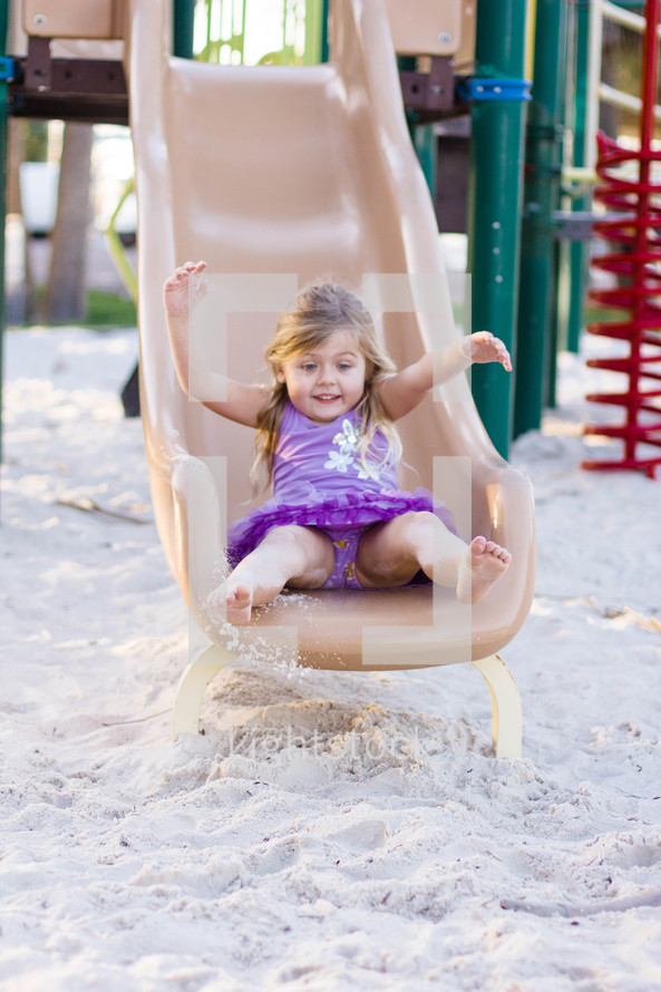Girl at the bottom of a slide with sand on her feet.