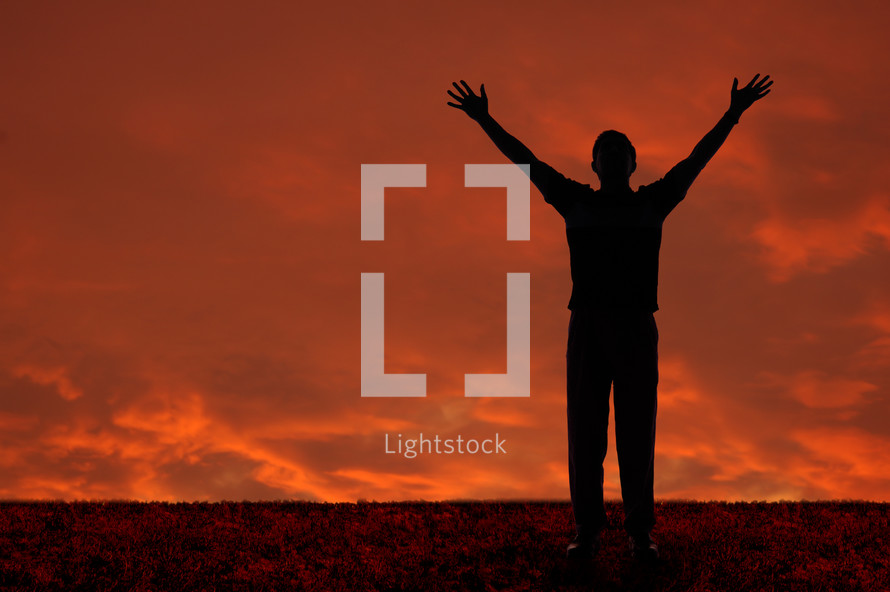 Silhouette of a man with arms raised praising God against and orange sky.