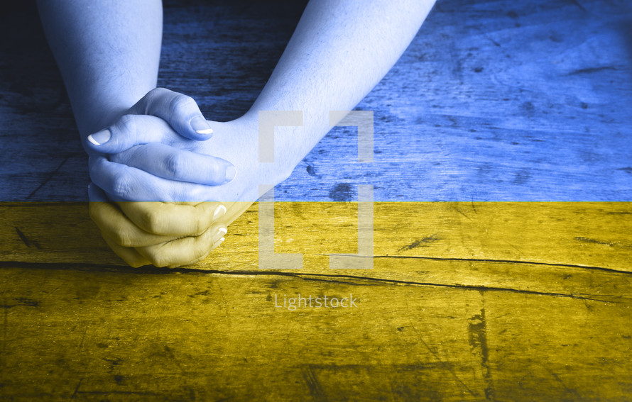 praying hands overlayed with the colors of Urkrainian flag 
