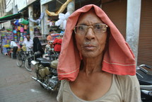 a man with a towel over his head standing in a street market 