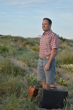 a man standing on a sandy hill with luggage 