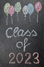 chalk on slate with balloons and the words: class of 2023