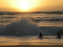 kids playing in the ocean at sunset 