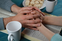 couple holding hands praying over open Bibles 