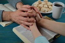 couple holding hands and praying over a Bible 