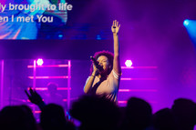 A woman singing on stage with her hand raised in worship.