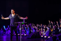 A congregation of worshippers near a stage with a worship leader.